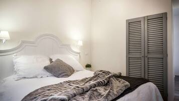 Un dormitorio con cama, candelabro, mesita de noche con lámpara y armario.