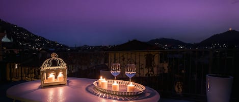 Mesa com velas e copos em terraço com vista para a cidade ao entardecer.