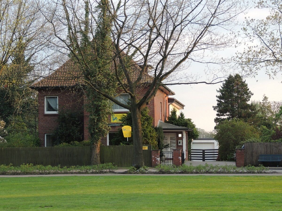 A two-story brick house with a visible garage door, surrounded by a well-maintained lawn and a wooden fence.