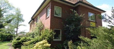 A two-story brick house with a tiled roof, surrounded by lush greenery and a well-maintained garden.