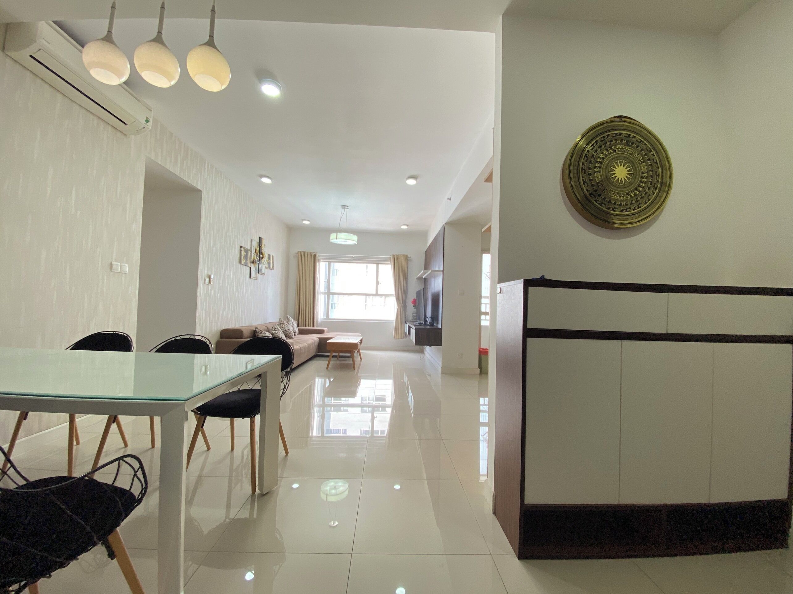 A modern living room with a glass dining table, a sofa, and a decorative wall piece.