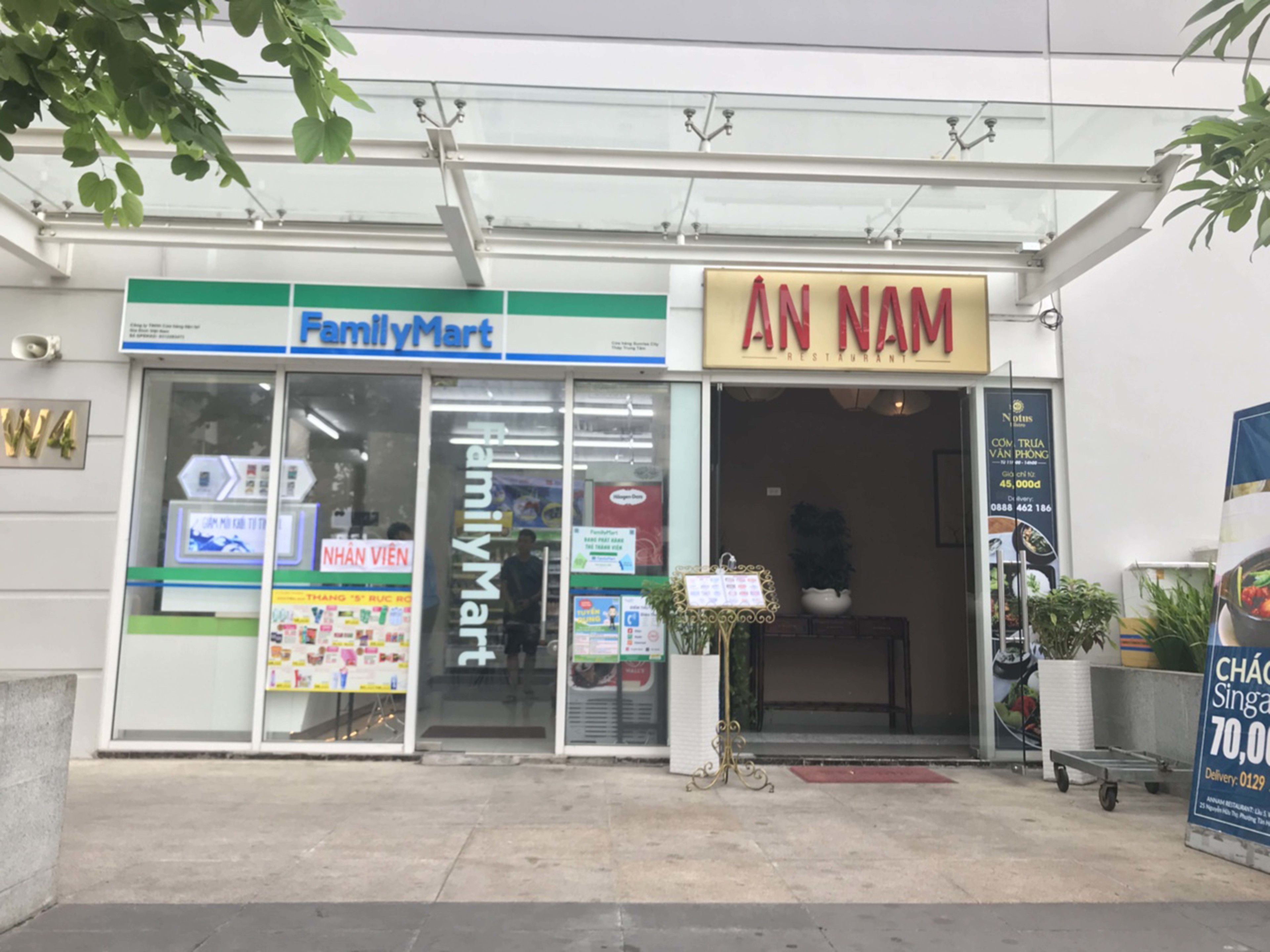 A FamilyMart and AN NAM restaurant storefront with a clear entrance, a signboard, and a delivery service advertisement.