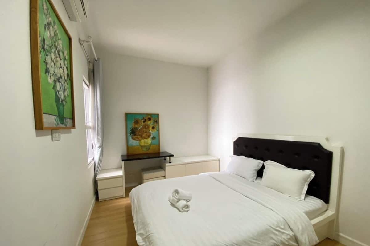 Een slaapkamer met een bed, nachtkastje, bureau en een schilderij aan de muur.