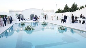 A pool area with white walls and a clear blue pool, surrounded by guests and floral arrangements.