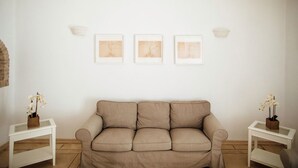 A neutral-toned living room with a beige sofa, two white side tables, and three framed artworks on the wall.