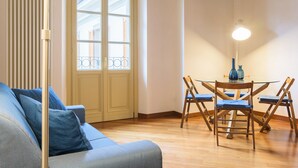 Un salon avec un canapé, une table à manger avec des chaises, une fenêtre avec des stores et un radiateur.