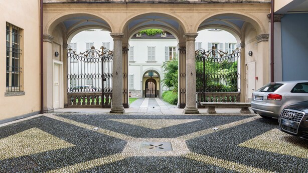 Une cour dallée de pierres, une arche centrale et une voiture garée sur le côté droit.