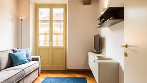 Un espace de vie compact comprenant un canapé, un téléviseur posé sur un meuble et une porte avec des fenêtres.