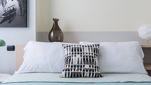 A neatly made bed with white linens and a patterned pillow, a vase on the nightstand, and a framed picture on the wall. - Domus (Como)