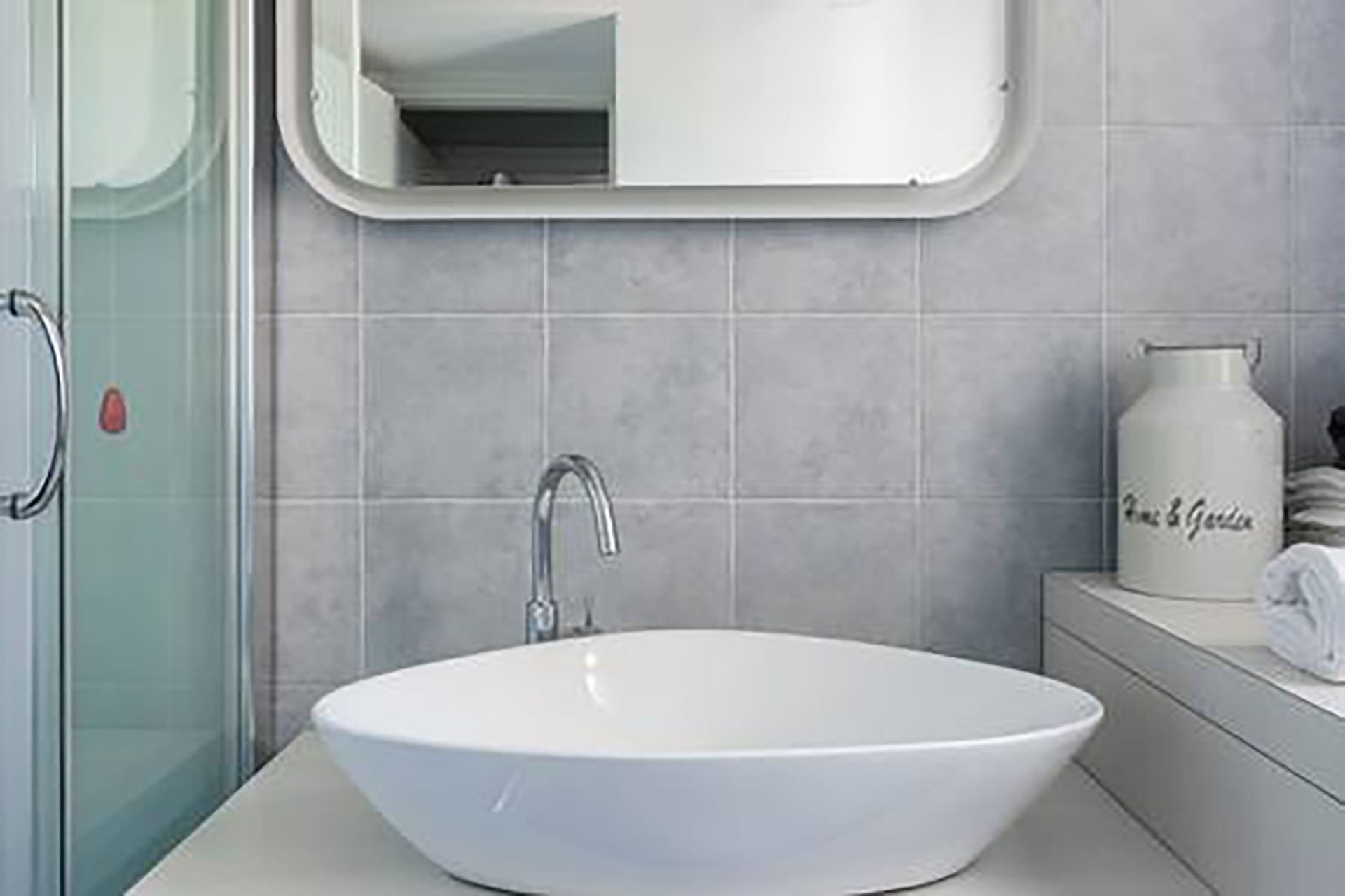 Une salle de bain avec un lavabo blanc, un miroir et un vase blanc posé sur le comptoir.