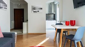 A modern living room with a sofa, a dining table with chairs, and a kitchen area with a microwave. - Domus (Como)