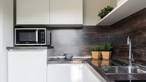 A modern kitchen with white cabinets, a built-in microwave, a stainless steel sink, and a dark backsplash. - Domus (Como)