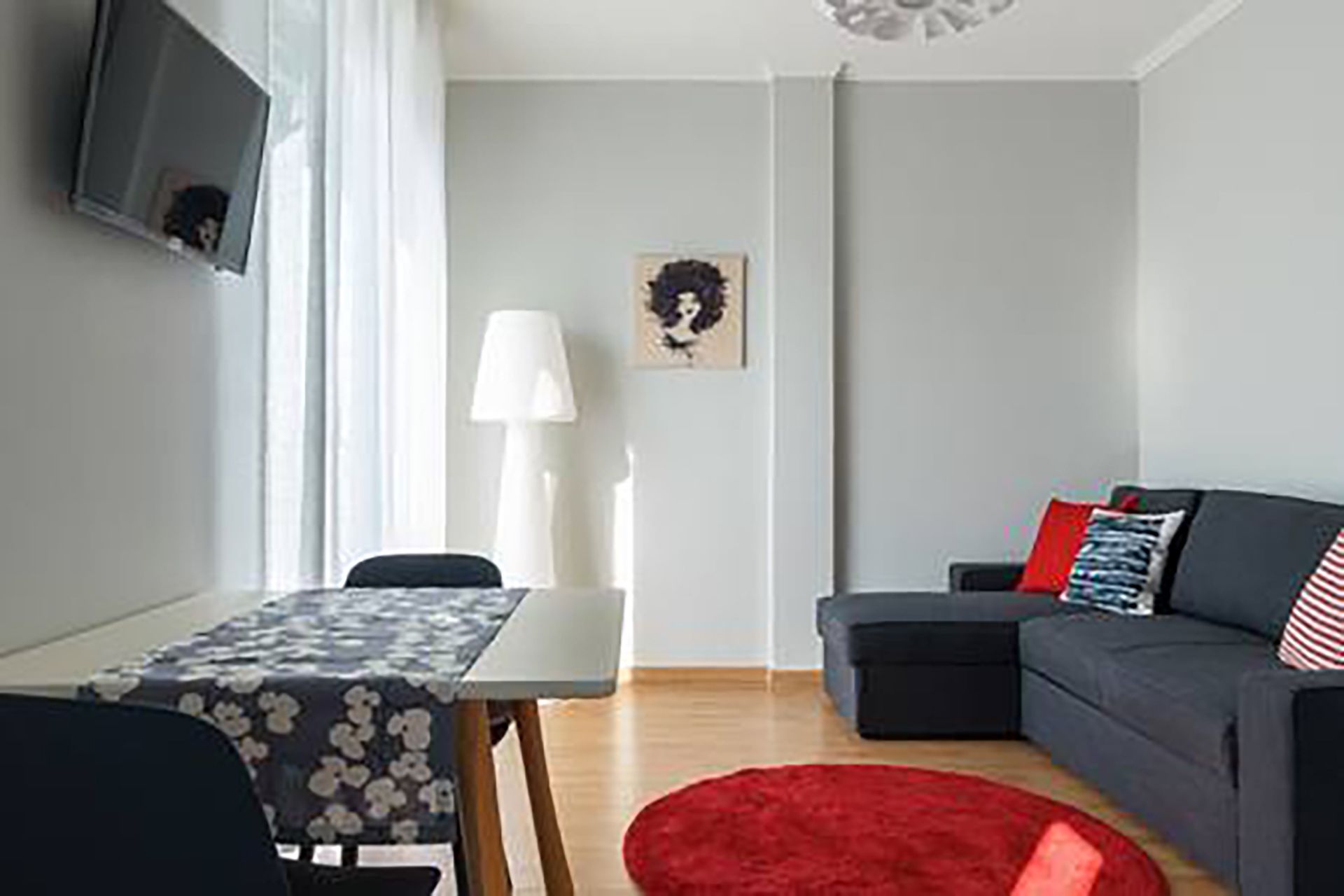 A modern living room with a grey sofa, a red rug, a white table, and a TV mounted on the wall.