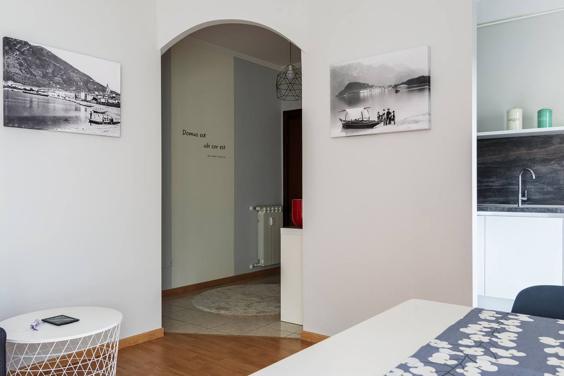 A modern hotel room with a wooden floor, a white round table, a bed with a floral bedspread, and two black-and-white photographs on the walls.