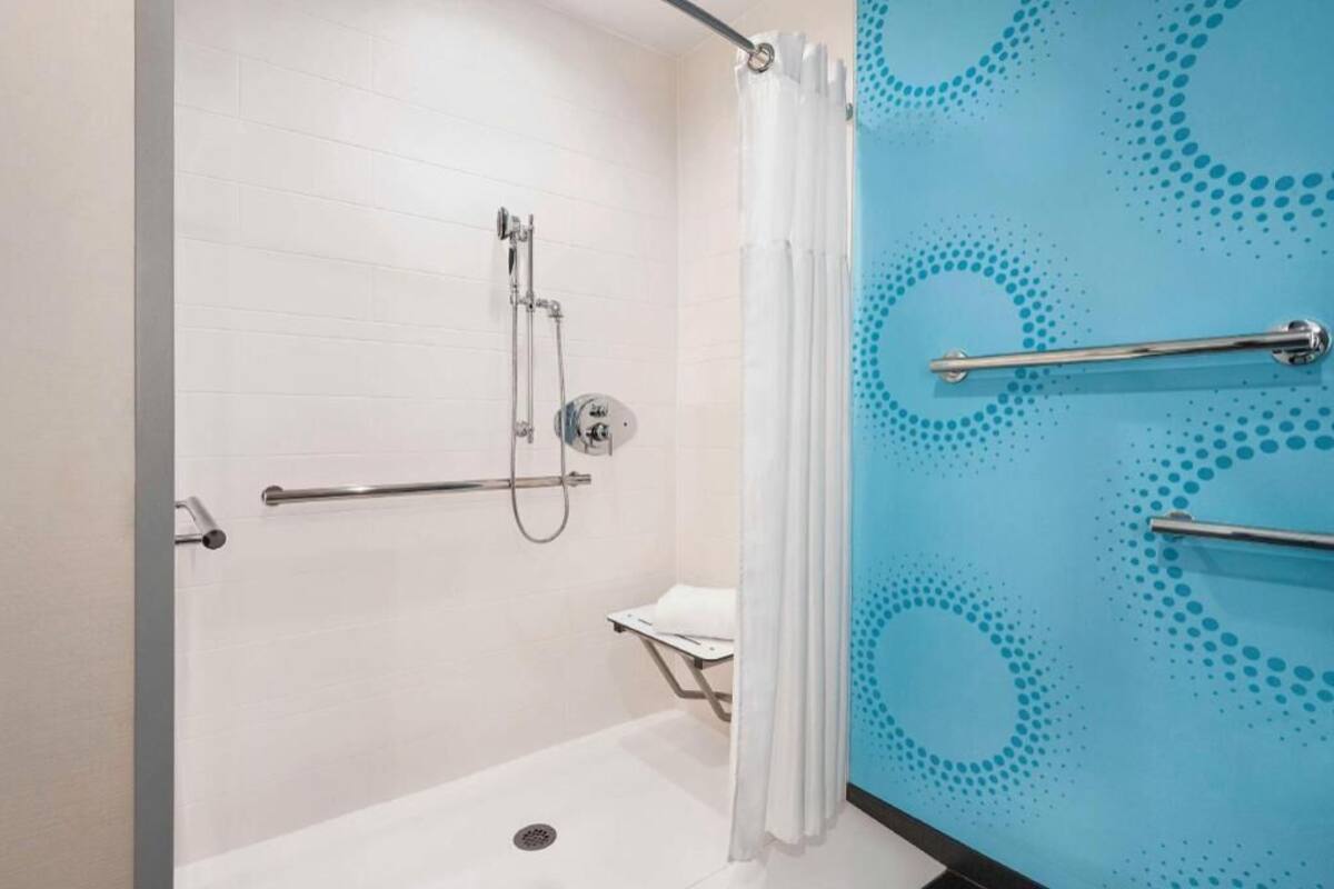 A shower area with a handrail, a showerhead, and a curtain.