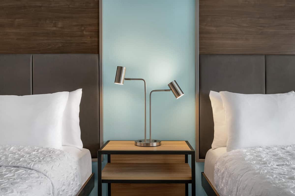 A hotel room with two beds, a nightstand with a modern lamp, and a wooden headboard.