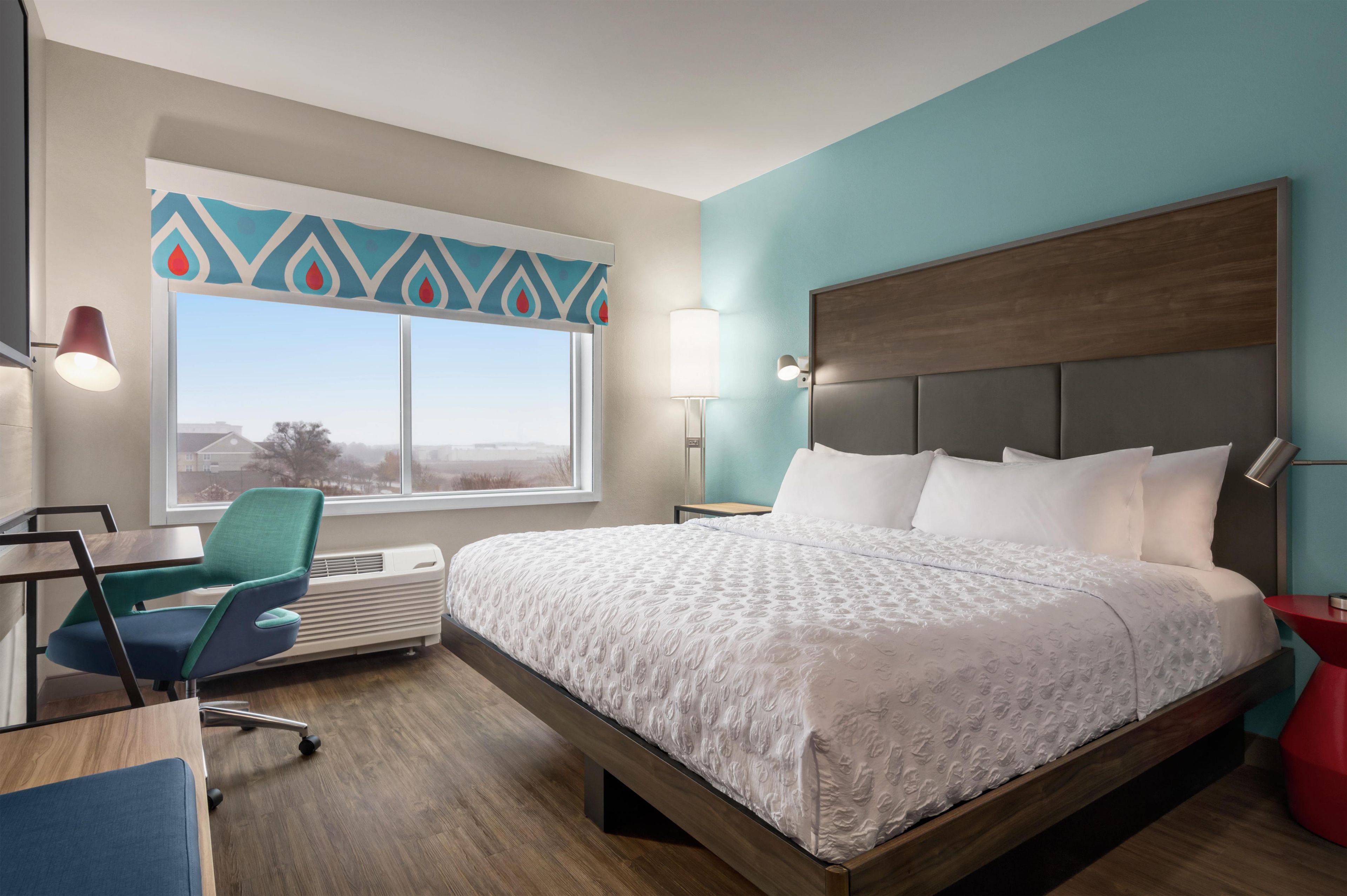 A hotel room with a bed, desk, chair, and a window with a view.