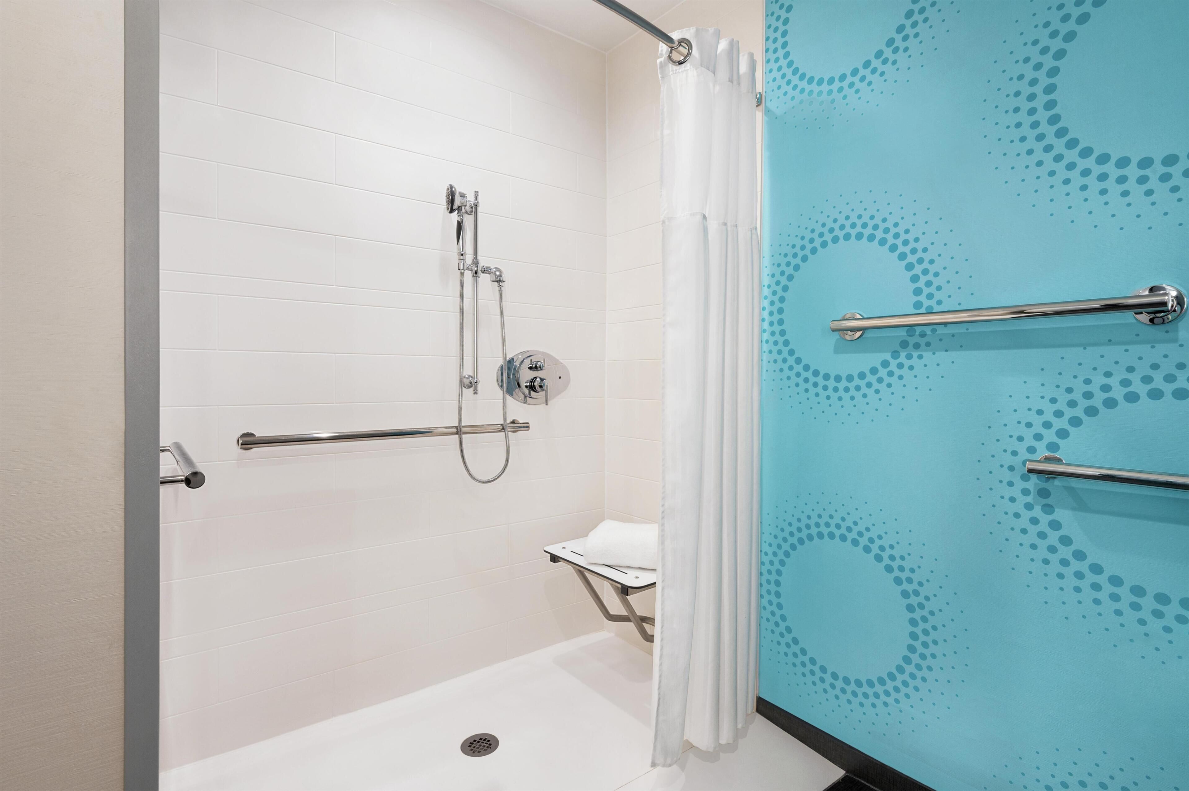 Een douche met een handdouche, een handdouche, een handgreep en een witte handdoek op een plank.