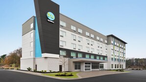 Een modern hotelgebouw met een opvallend logo, meerdere verdiepingen en een overdekte ingang.