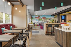A restaurant with a mural, wooden tables, and a bar area. - Tru by Hilton Greenville Woodruff Road (Greenville)