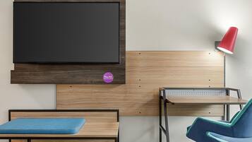A room with a bed, a desk, a chair, a TV mounted on the wall, and a red lamp.