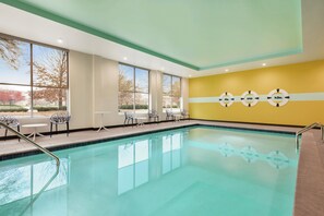 Una piscina con agua cristalina, rodeada de ventanales y un muro amarillo con símbolos de seguridad.