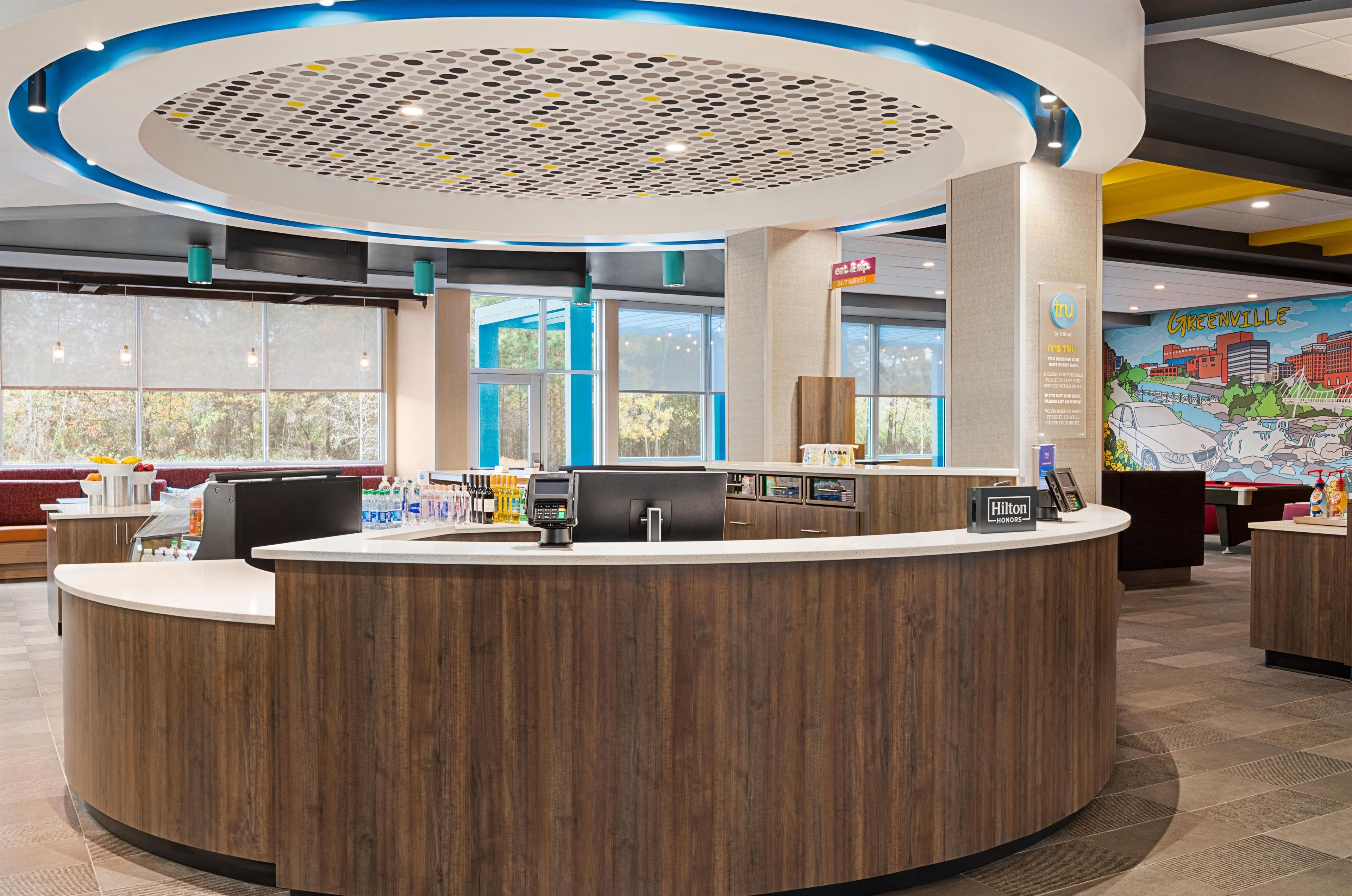 Een hotel receptie met een houten balie, een digitaal scherm en een muurschildering van Greenville.