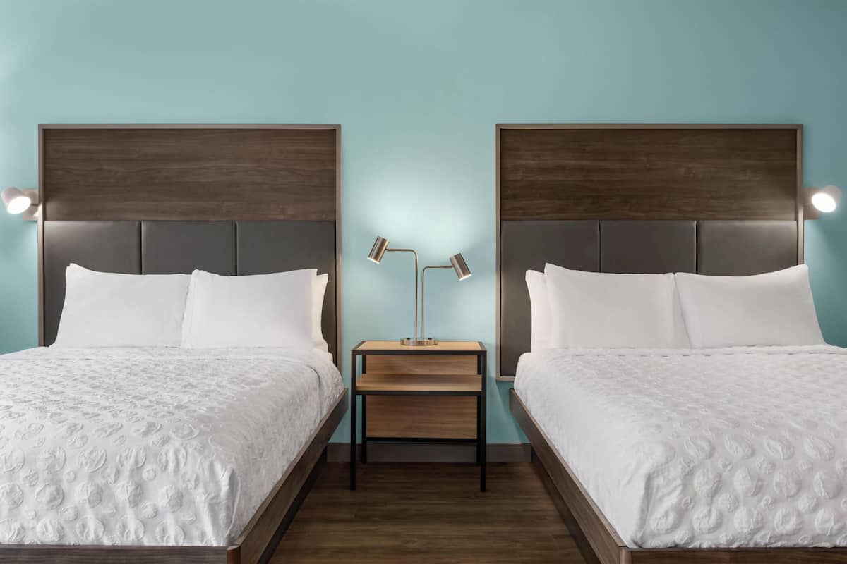 A twin room with two beds, a nightstand with a lamp, and a light blue wall.
