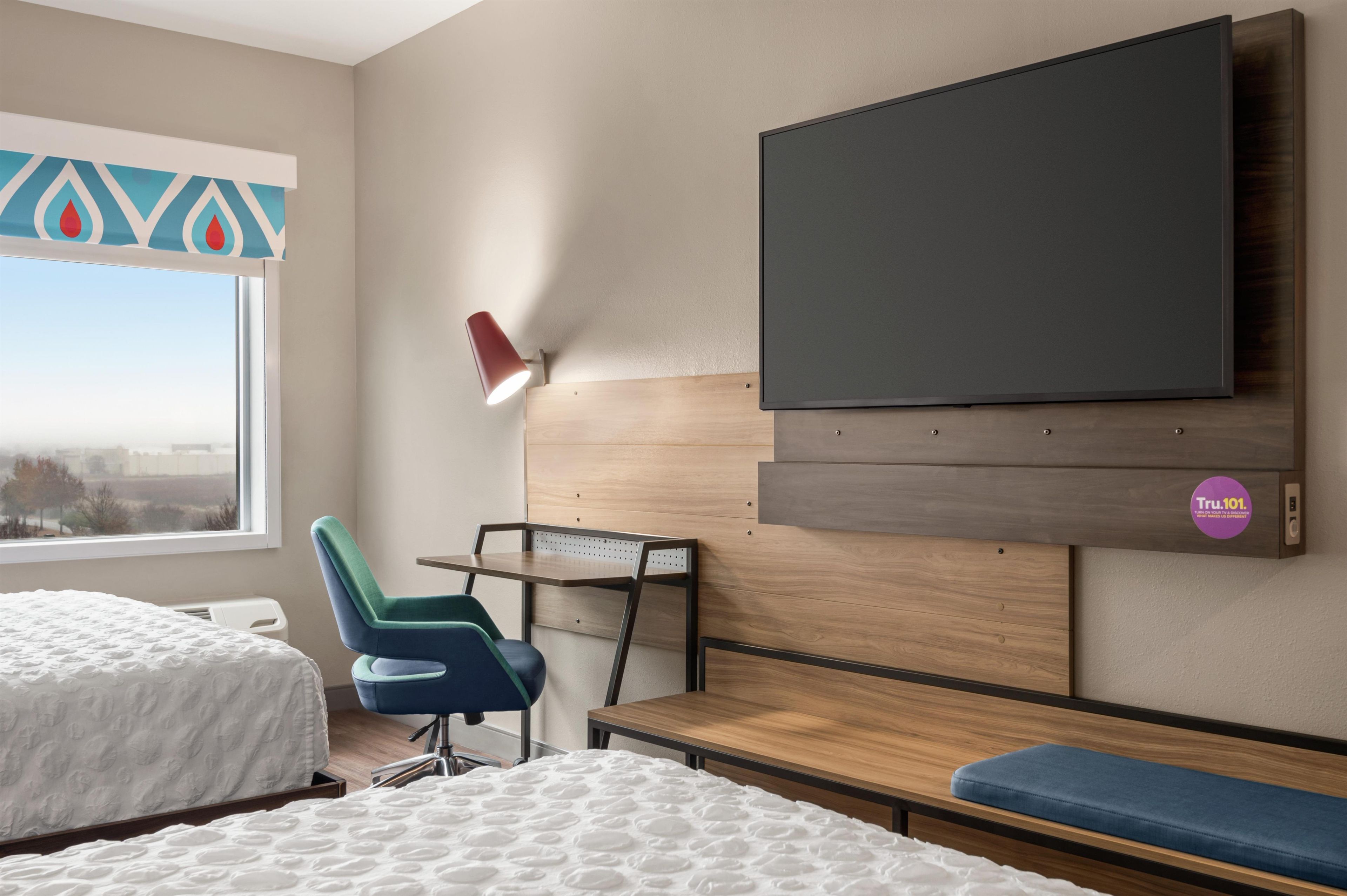 Une chambre d’hôtel avec un lit, un bureau, une chaise, une télévision et une fenêtre.