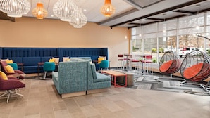 Een moderne lobby met een blauwe bank, blauwgroene fauteuils, hanglampen en een zithoek met ronde stoelen.