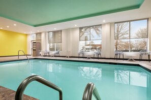 Una piscina interior con paredes de vidrio transparente, una pared amarilla en un lateral y vistas a un edificio exterior.