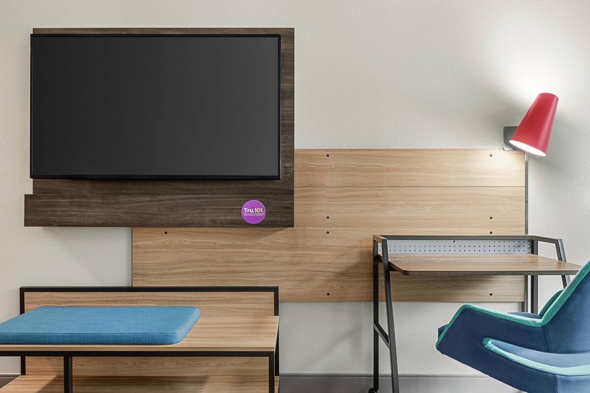 A room with a bed, a desk, a chair, a TV mounted on the wall, and a red lamp.