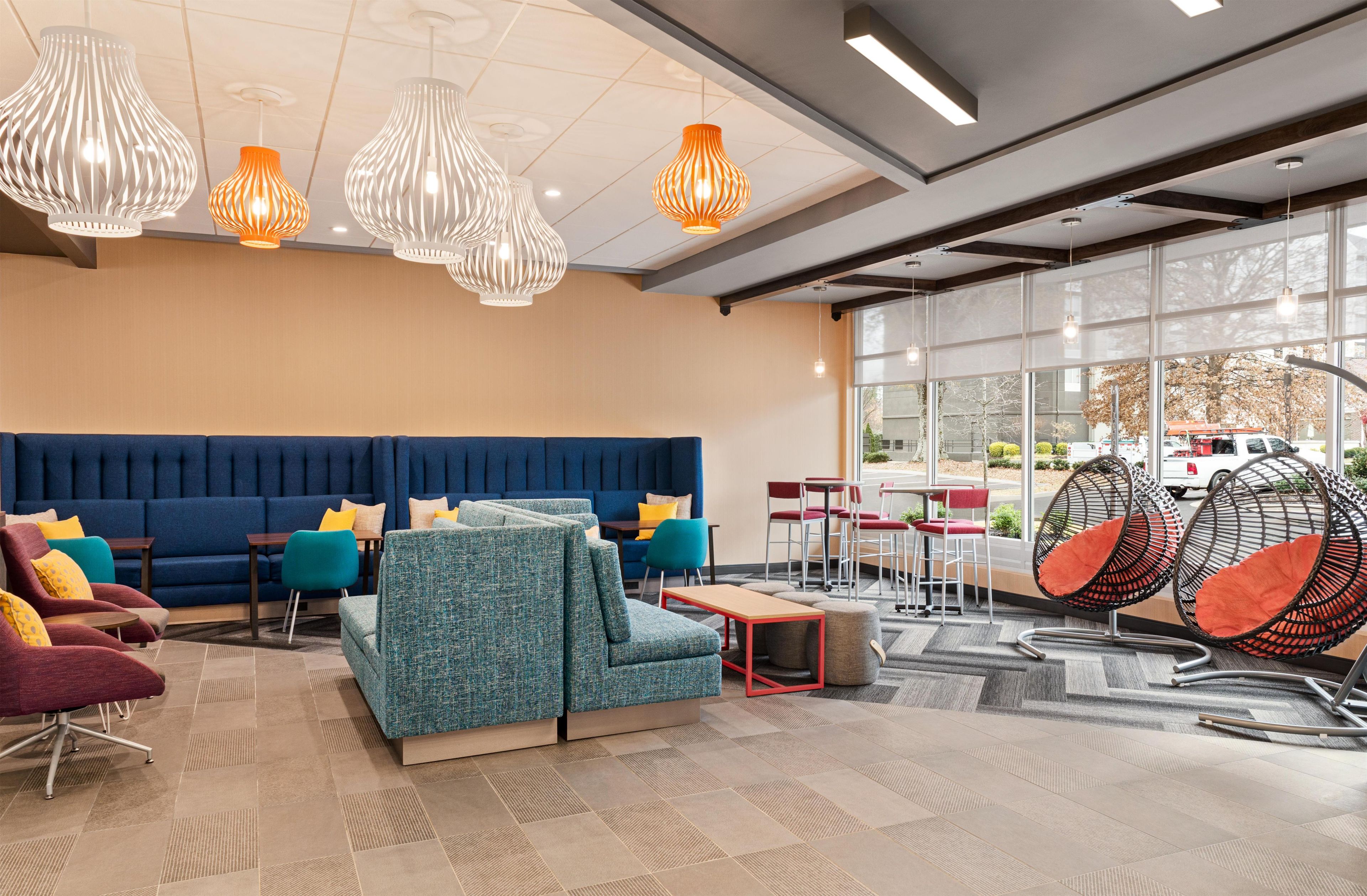 A modern lobby with a blue sofa, teal armchairs, hanging lights, and a seating area with round chairs.