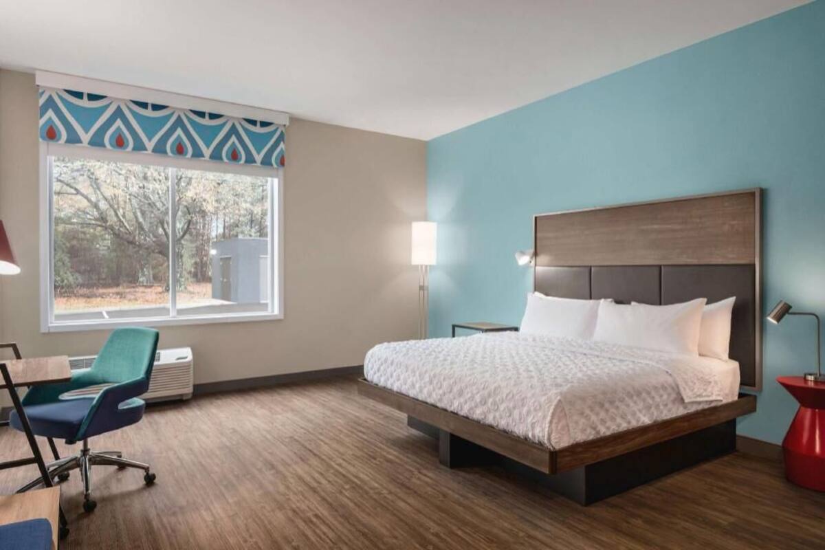 Ein Hotelzimmer mit Bett, Schreibtisch, Stuhl, Fenster mit Blick und Lampe.