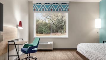 Ein Hotelzimmer mit Bett, Schreibtisch, Stuhl, Heizung und Fenster mit Blick auf Bäume.