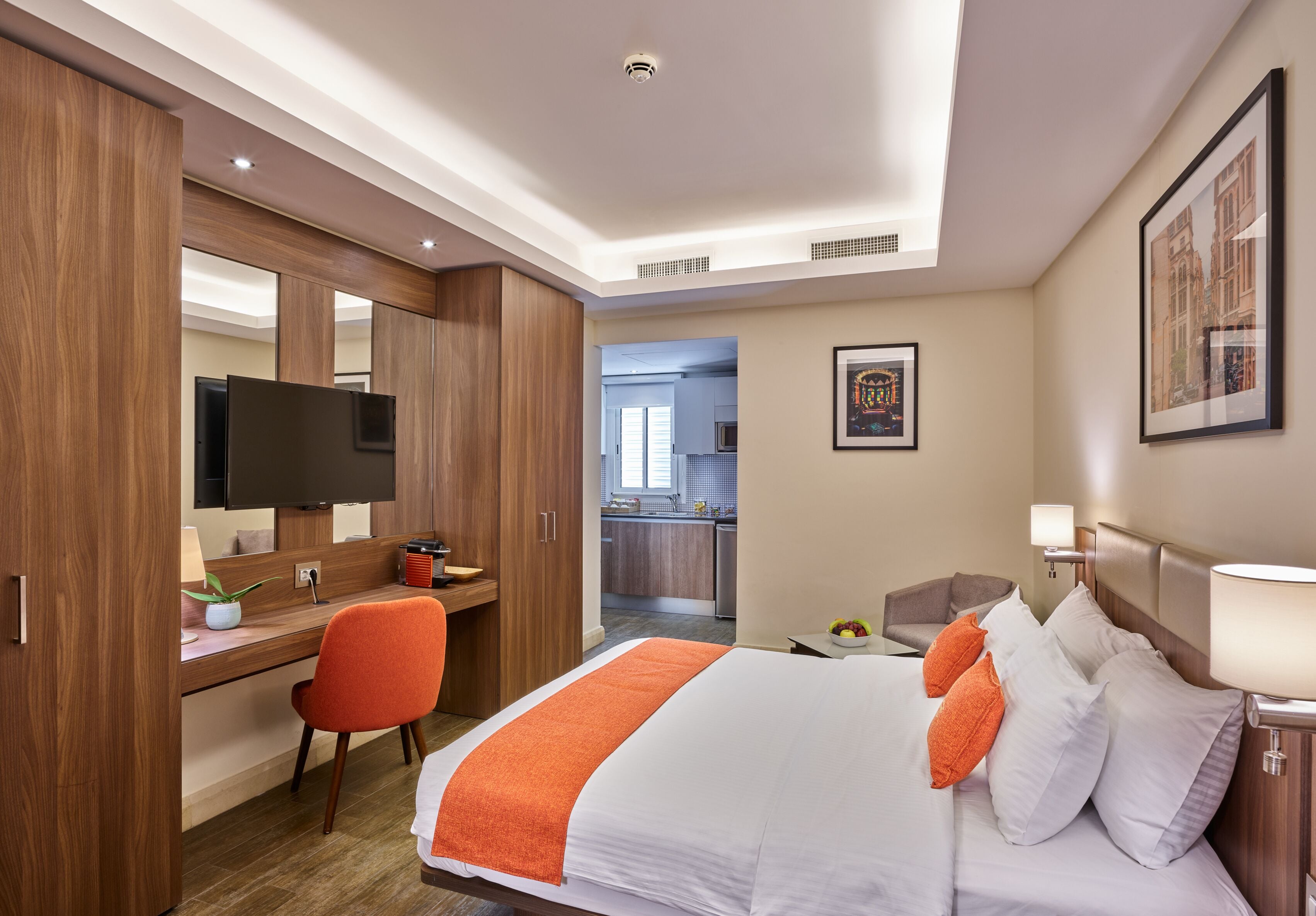 Habitación de hotel con cama, escritorio, silla, televisor y vista a la cocina.