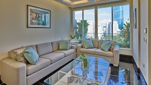 A modern living room with a beige sofa, a glass coffee table, and a large window offering a city view. - Sodeco Suites (Beirut)