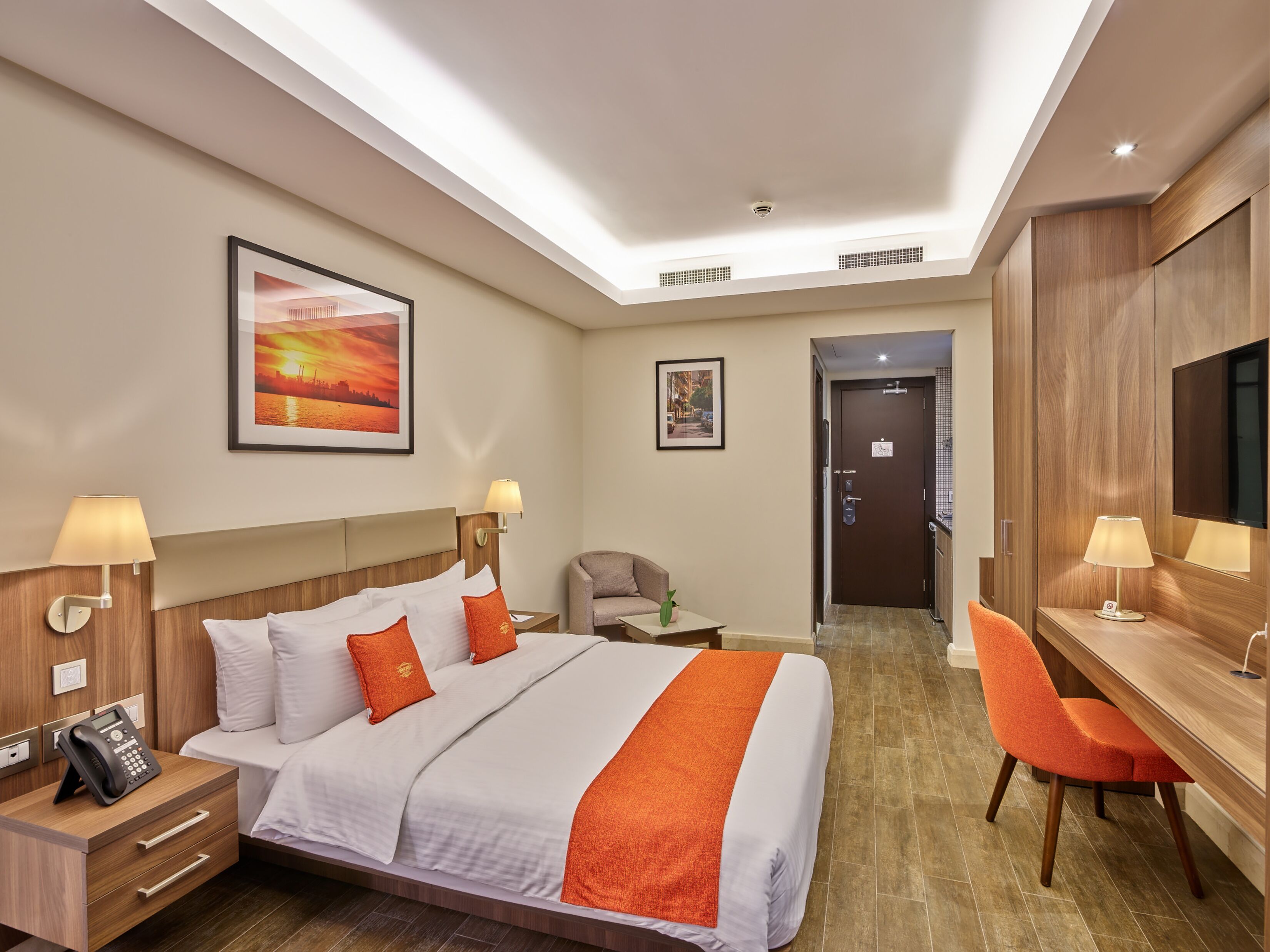 Habitación de hotel con cama, mesitas de noche, escritorio, silla y cuadros en las paredes.
