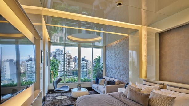 A modern bedroom with a large bed, a sofa, and a dining table. It features large windows with a city view. - Sodeco Suites (Beirut)