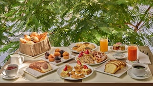 A breakfast table with various pastries, fruits, and beverages, set outdoors with lush greenery in the background. - Sodeco Suites (Beirut)