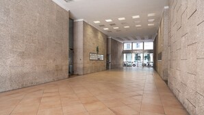 A spacious corridor with tiled flooring and stone walls, leading to a building entrance with large windows. - Casa Laurino B&B (Naples)