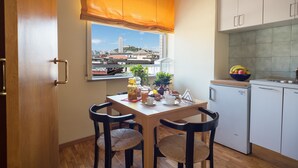A small kitchen with a dining table, chairs, a refrigerator, and a window with a view of buildings. - Casa Laurino B&B (Naples)