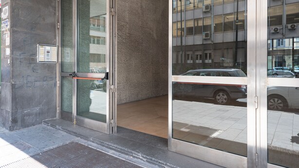 A building entrance with a glass door, a metal handle, and a small window with a sign. - Casa Laurino B&B (Naples)