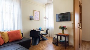A compact living space with a sofa, a dining table, a TV, and a small side table with flowers. - Casa Laurino B&B (Naples)