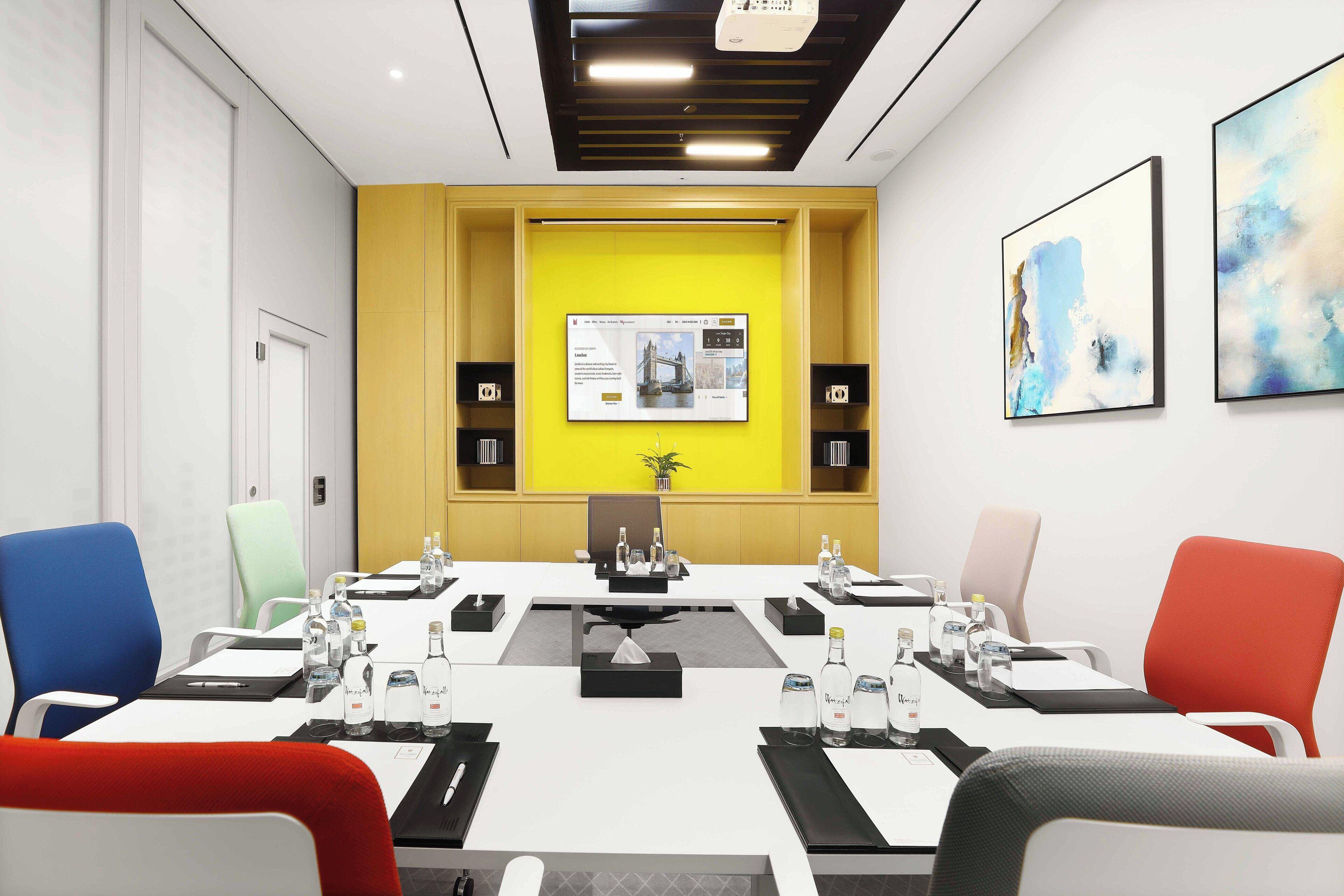 A conference room with a long table, multiple chairs, and a yellow accent wall.