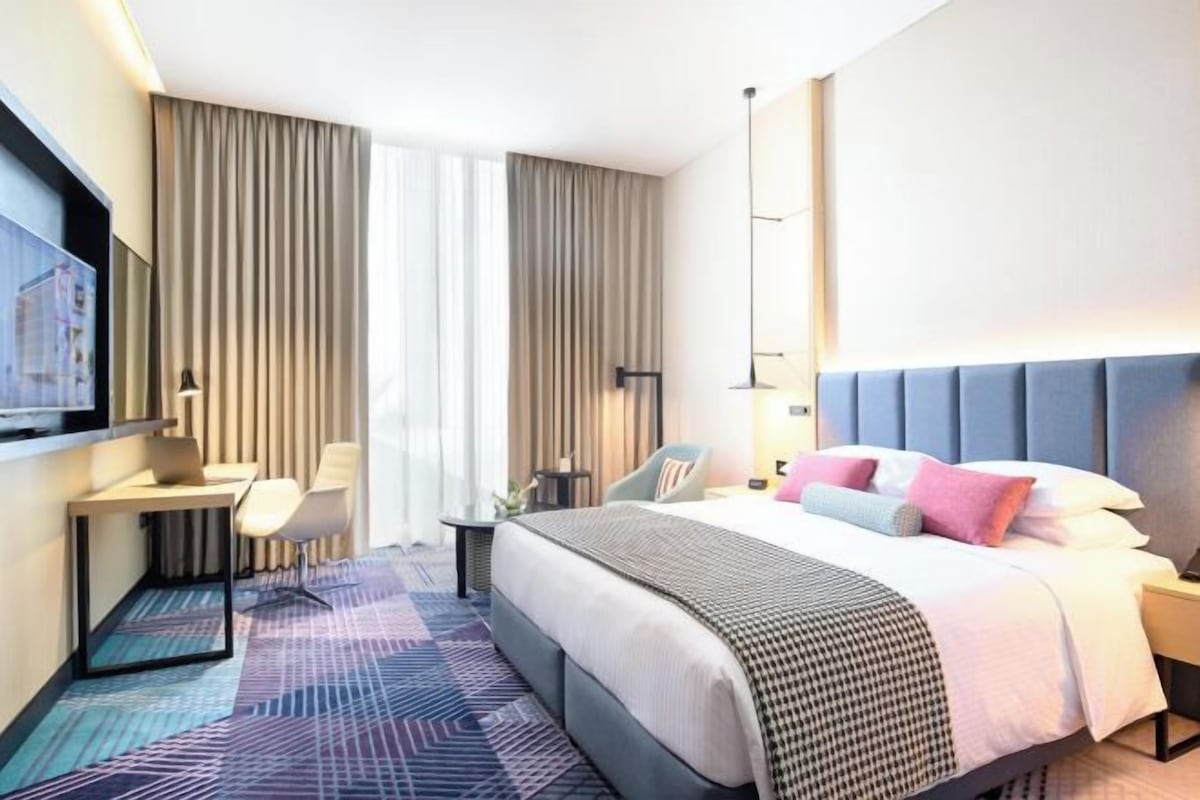 A modern hotel room with a large bed, a desk, and a chair.