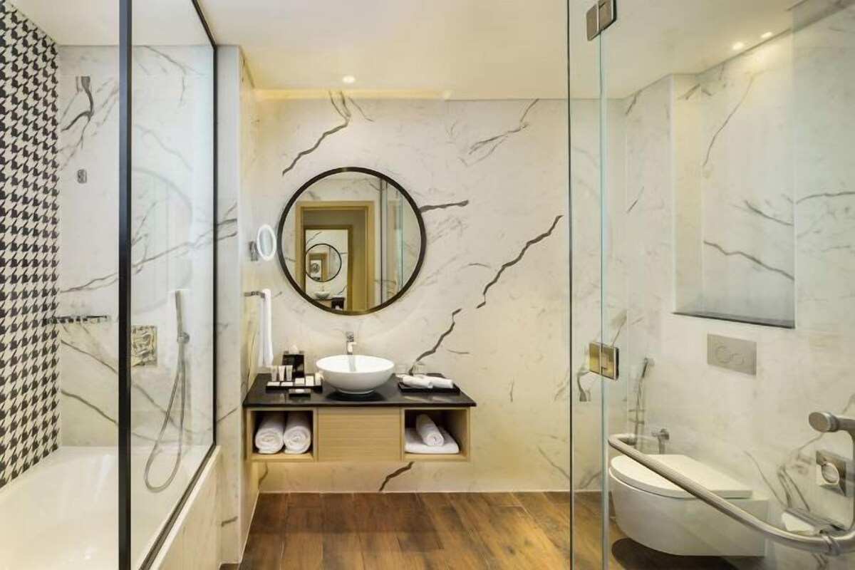 A modern bathroom with a glass-enclosed shower, a round mirror, a white sink, and a freestanding bathtub.
