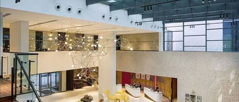 A spacious lobby with a high ceiling, a reception desk, a staircase, and a seating area with cushions and birdcages.