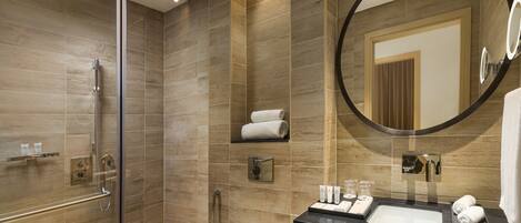 Un baño moderno con ducha envuelta en vidrio, tocador con lavamanos y un espejo grande.