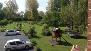 Un jardin avec une cabane en bois, un trampoline et une voiture blanche garée au premier plan.